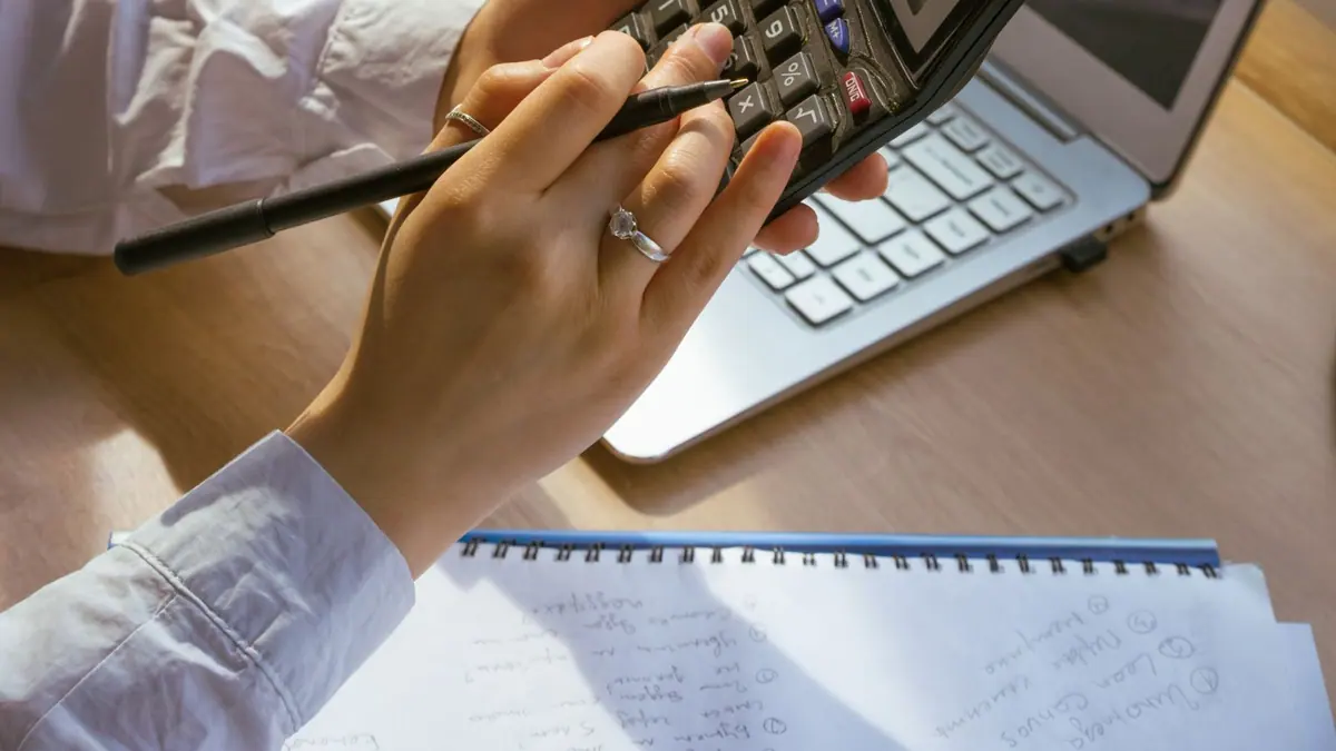 Mains utilisant une calculatrice devant un ordinateur et un carnet